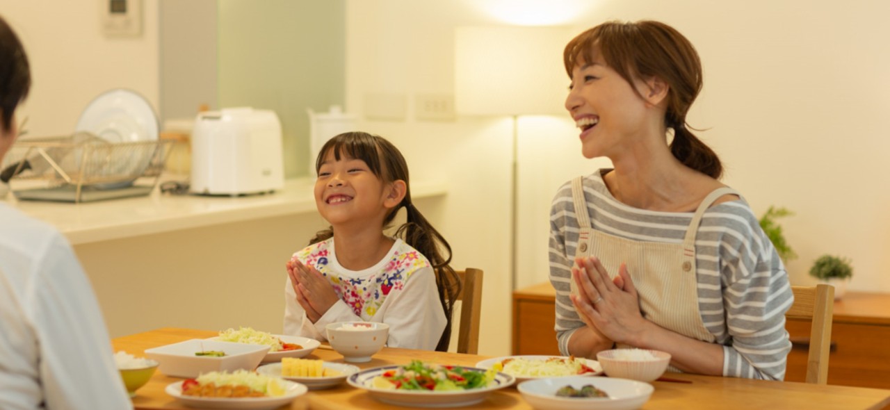 食卓でおいしいごはんをたのしむ家族の写真です。