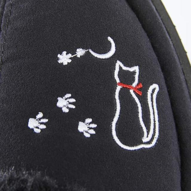 サンダルの甲に施された、赤いリボンを付けた白猫と足跡の刺繍のクローズアップ。